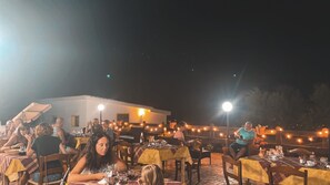 An outdoor dining area with tables and chairs, string lights, and a building in the background. - Agriturismo Paulesa (Dorgali)