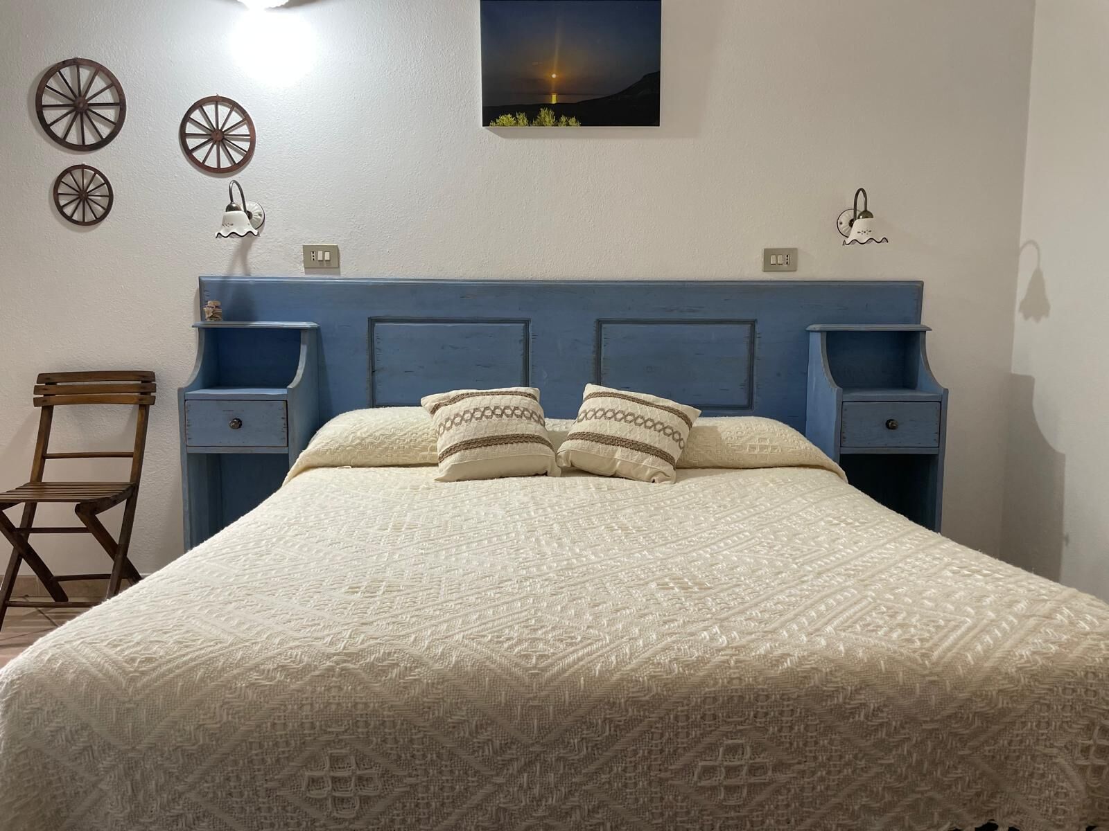 Un dormitorio con una cama grande, dos mesitas de noche, una silla y elementos decorativos en la pared.