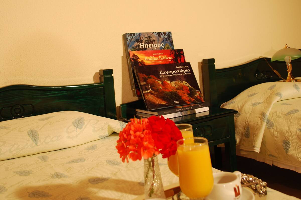 A hotel room with a bed, a painting on the wall, a tray with breakfast items, and a book on the nightstand.