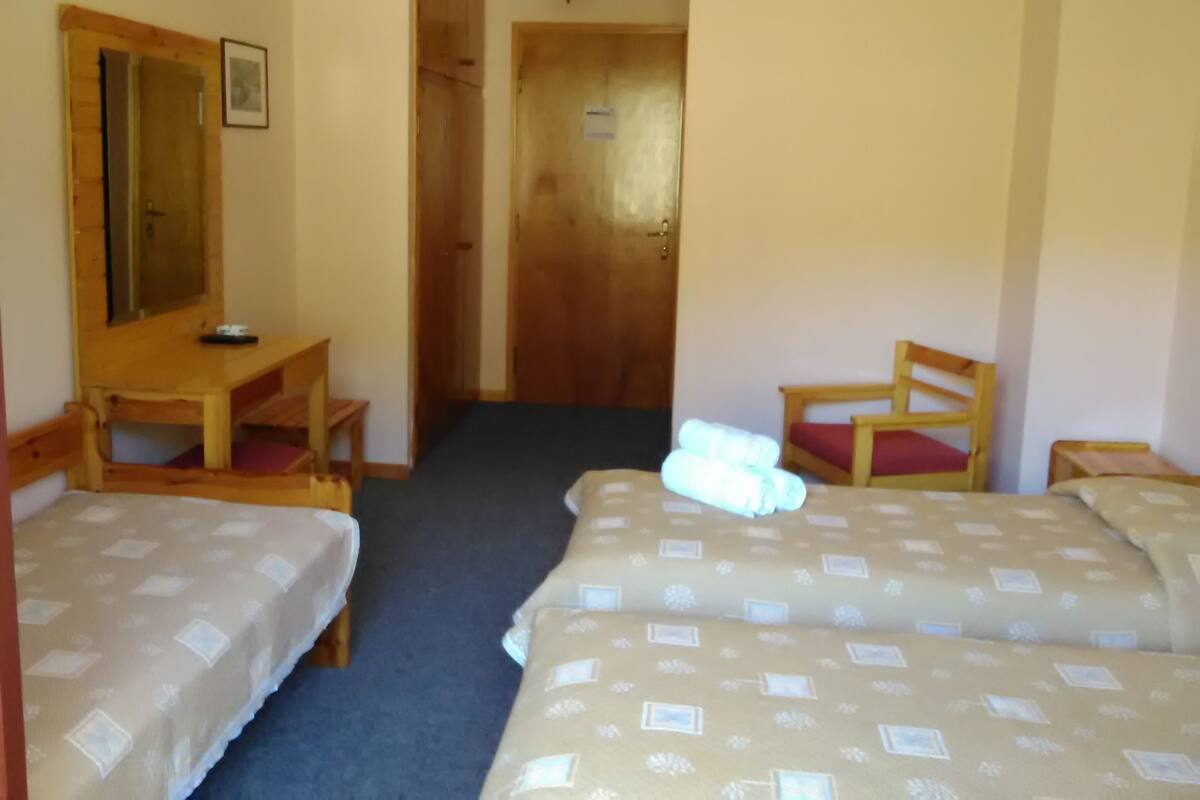 A room with two beds, a wooden desk, a chair, and a door.