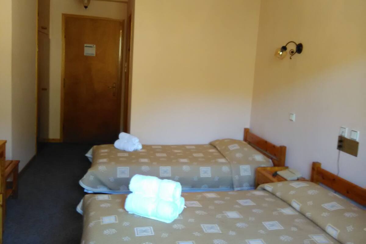 A hotel room with two beds, a wooden door, and a nightstand with a lamp.