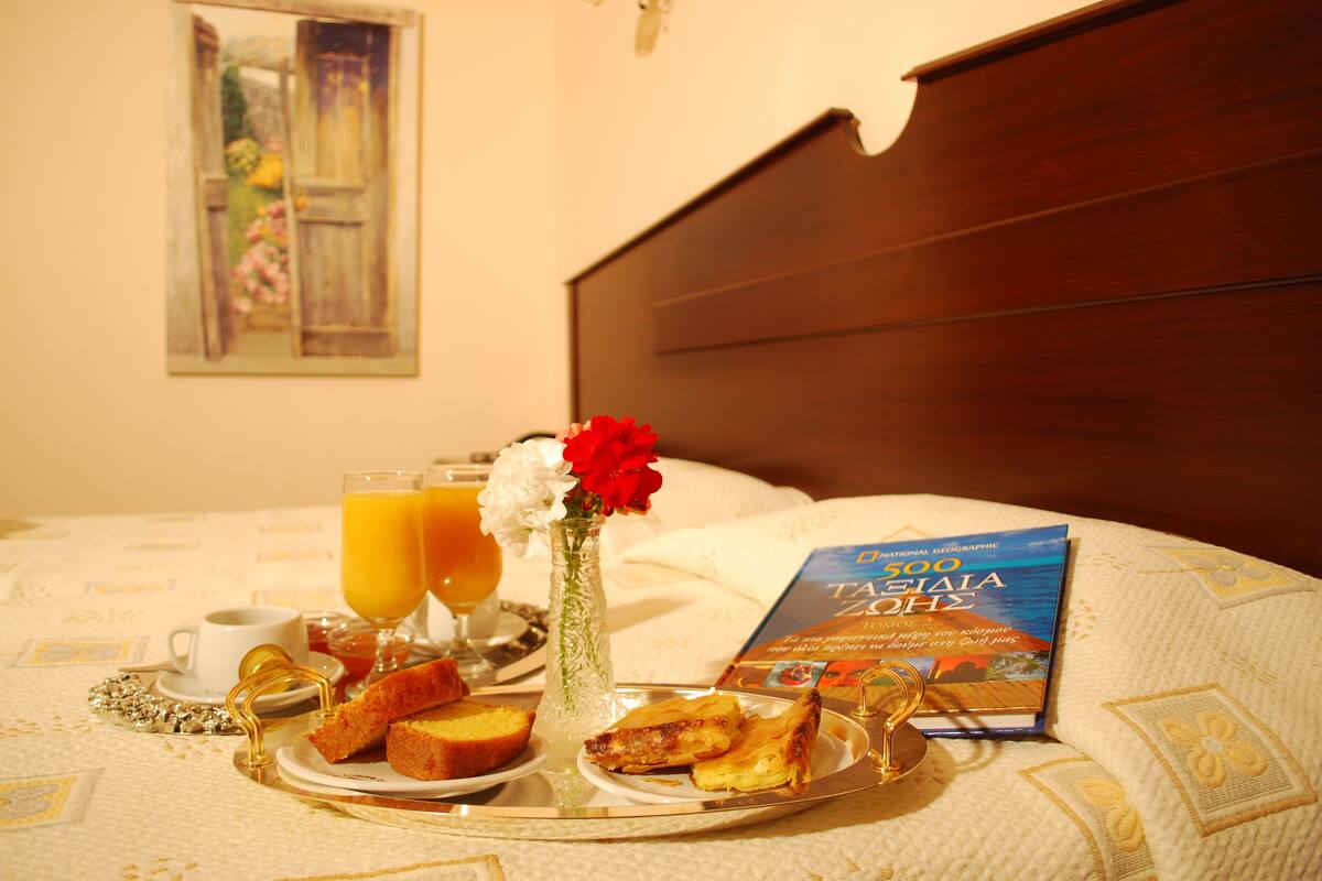 A breakfast tray with toast, juice, and a book on a bed with a wooden headboard.