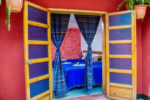 Una habitación con una cama, una mesa con mantel azul y una pared roja.