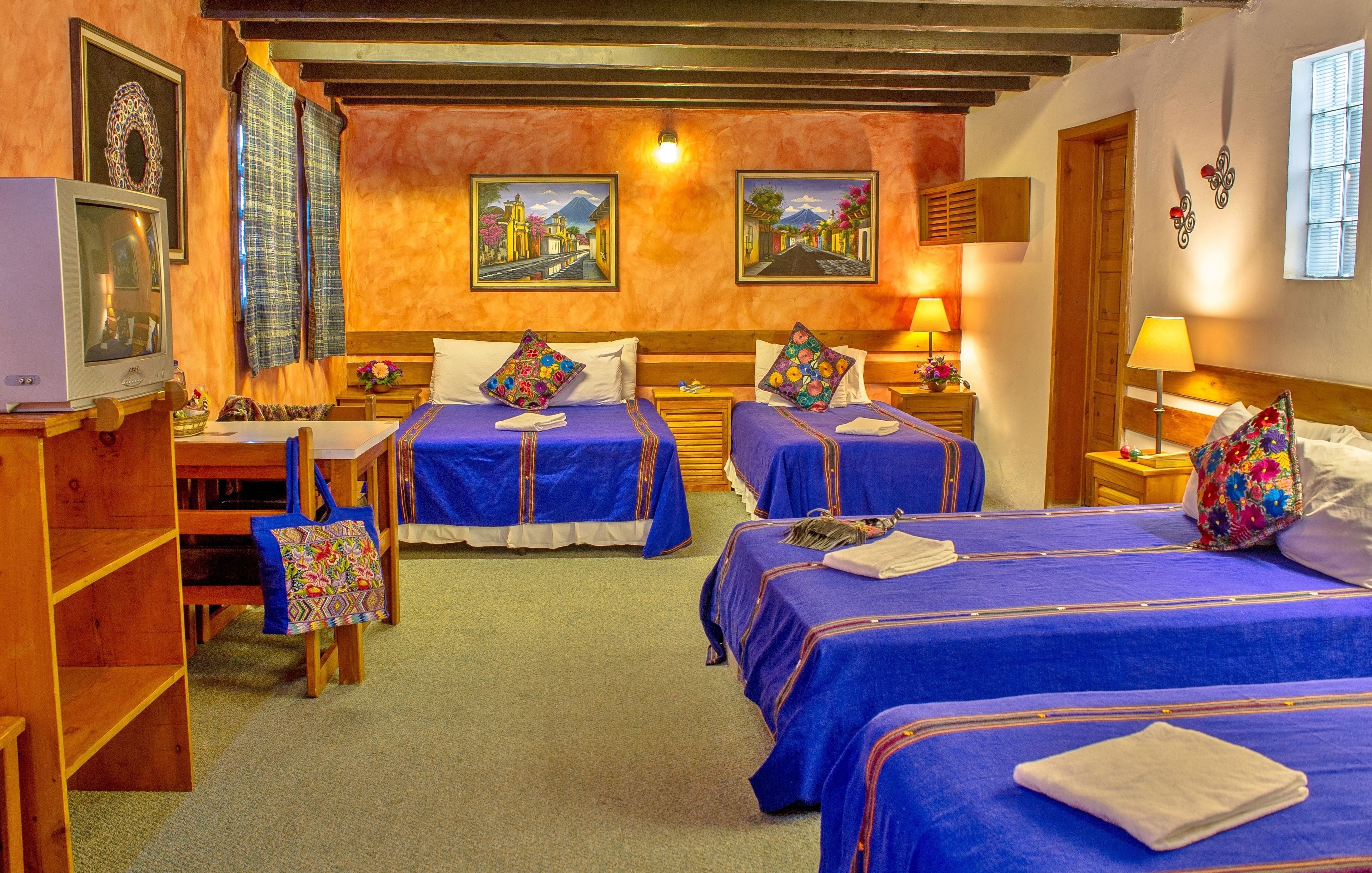 Een hotelkamer met drie bedden, een houten bureau, een stoel en een televisietoestel.
