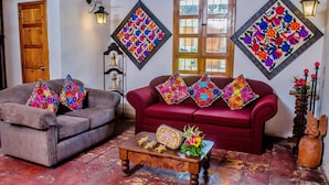 A cozy room with two sofas, a wooden coffee table, and floral wall art. - Hotel Panchoy (Antigua Guatemala)