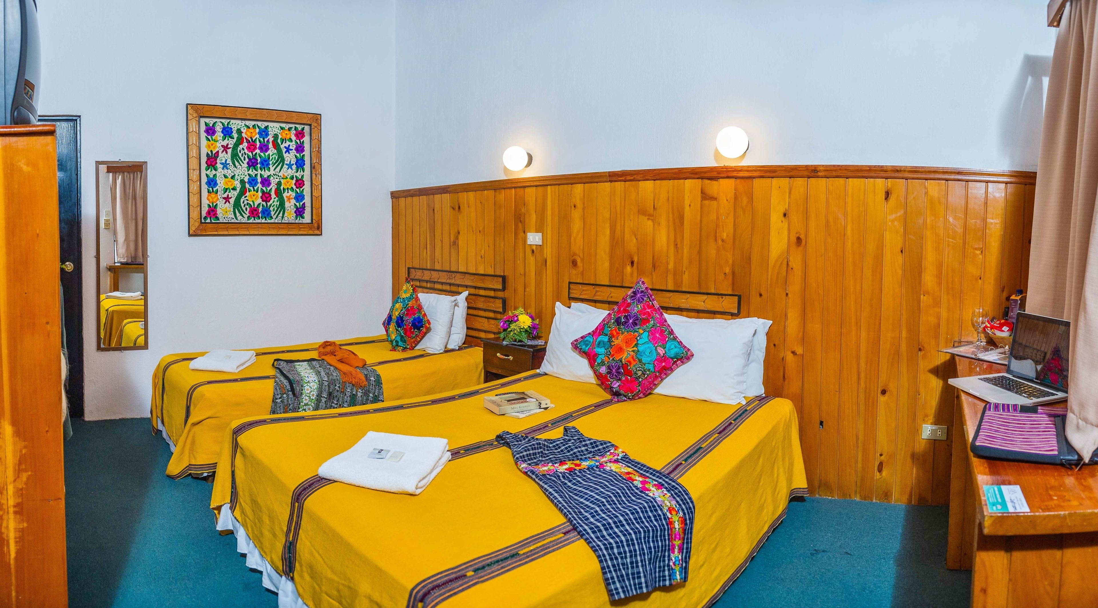 Une chambre d’hôtel avec deux lits, des têtes de lit en bois, un miroir, un tableau et un ordinateur portable posé sur un bureau.