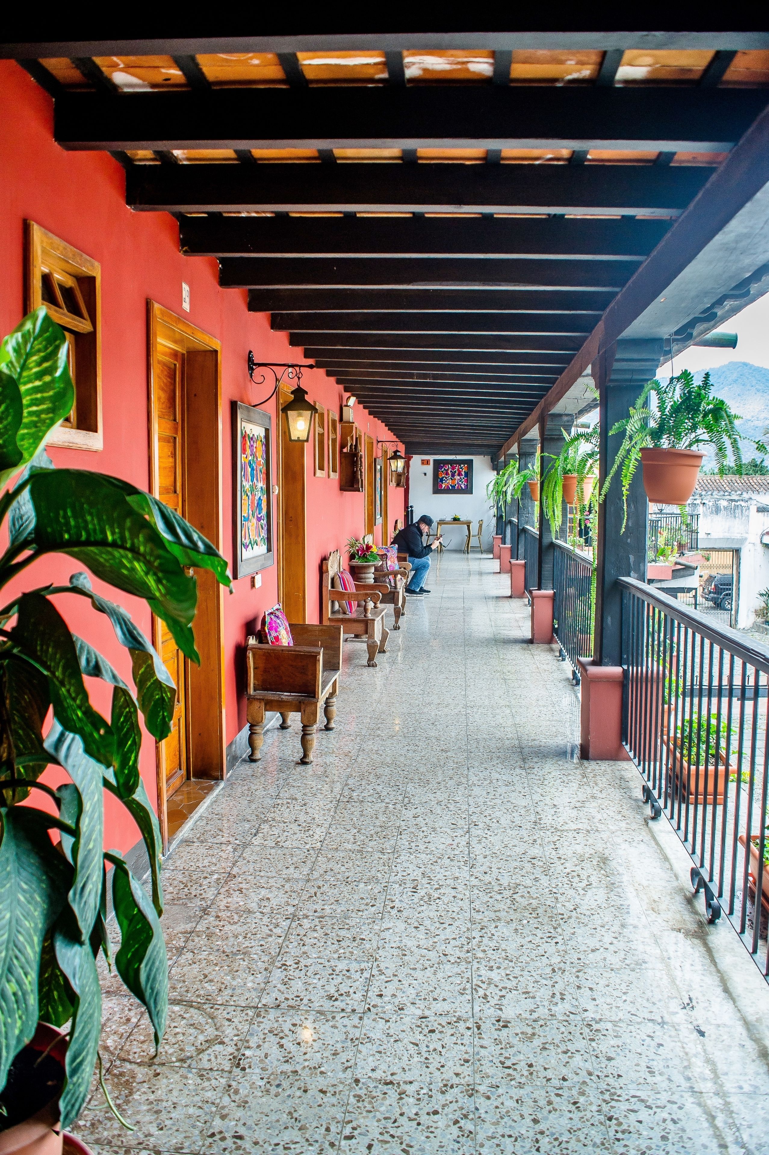 A covered corridor with wooden benches, potted plants, and a tiled floor.