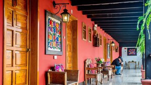A corridor with wooden doors, benches, and a person using a mobile phone. - Hotel Panchoy (Antigua Guatemala)