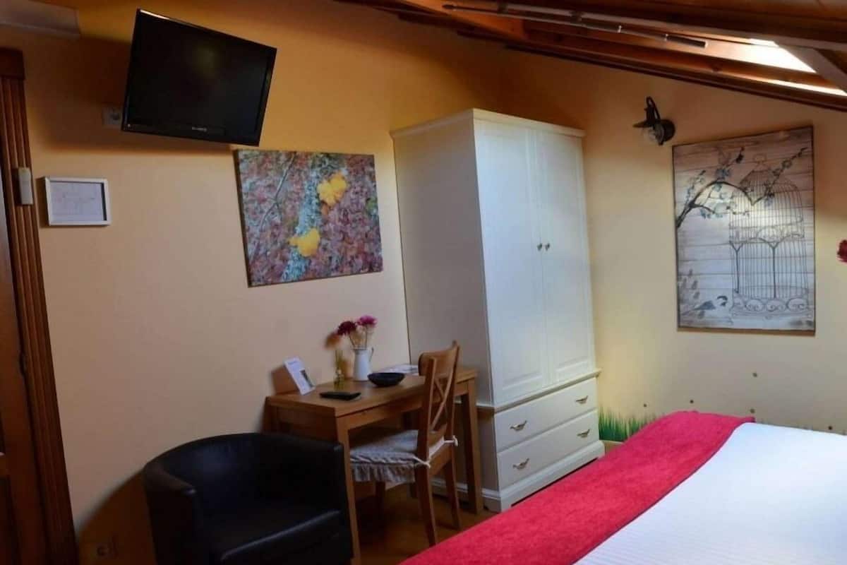 Une chambre à coucher comprenant un lit, un bureau avec une chaise, une armoire et deux téléviseurs fixés au mur.