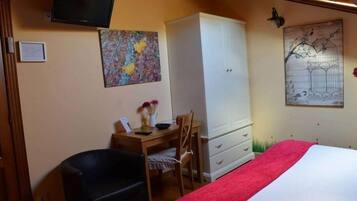 Un dormitorio con una cama, un escritorio con una silla, un armario y dos televisores instalados en la pared.