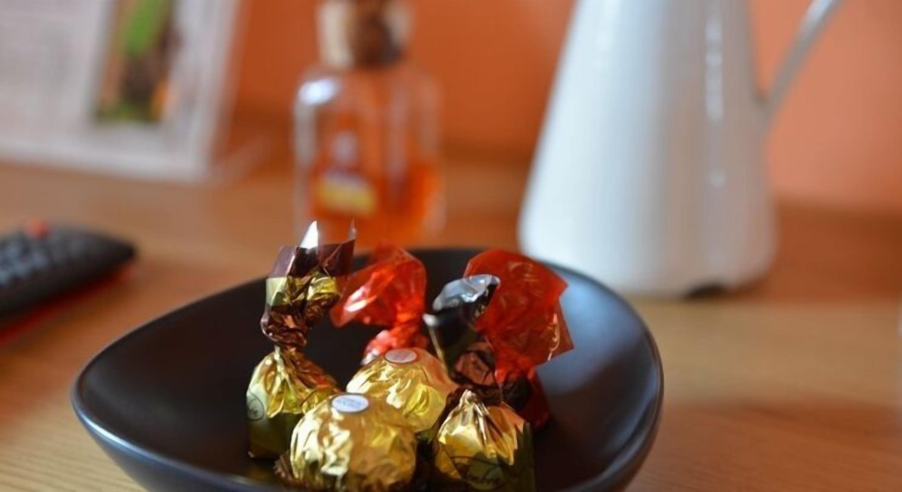 A black bowl containing several wrapped chocolates on a wooden table.