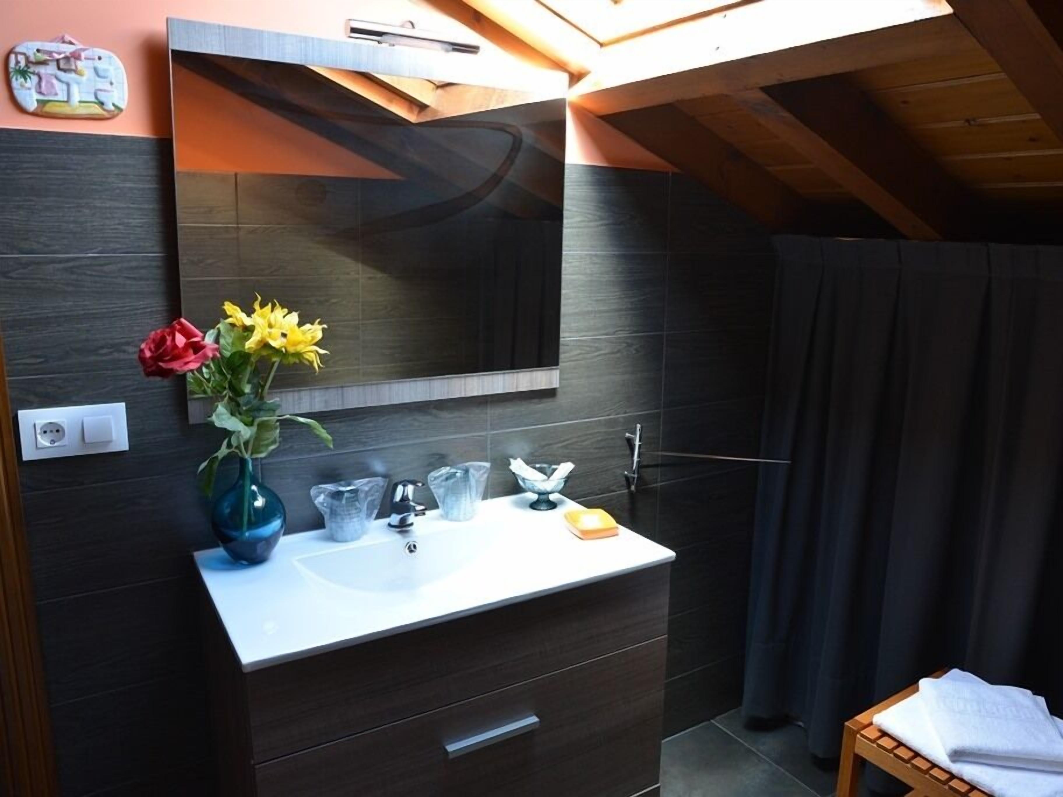 Un bagno moderno con un mobile lavabo in legno scuro, uno specchio grande e un vaso con fiori.