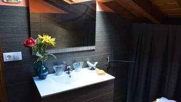 Un bagno moderno con un mobile lavabo in legno scuro, uno specchio grande e un vaso con fiori.