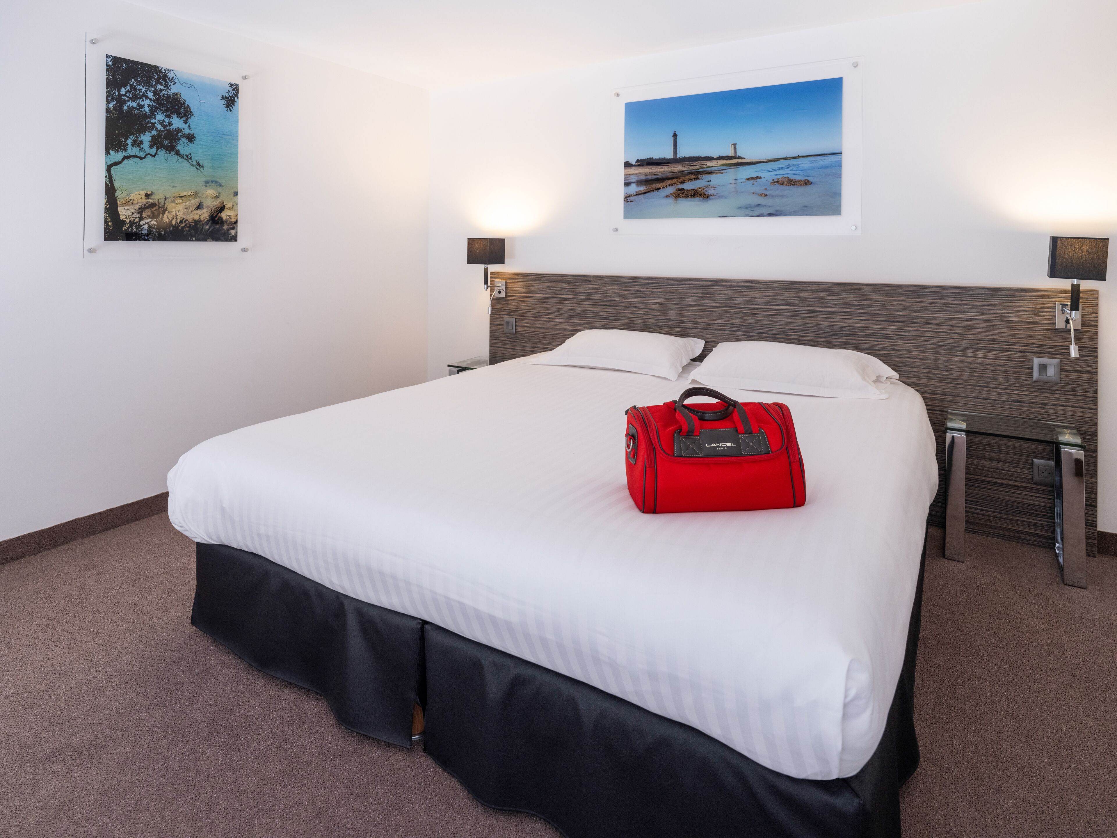 Una habitación de hotel con una cama, un bolso rojo y dos lámparas fijadas a la pared.