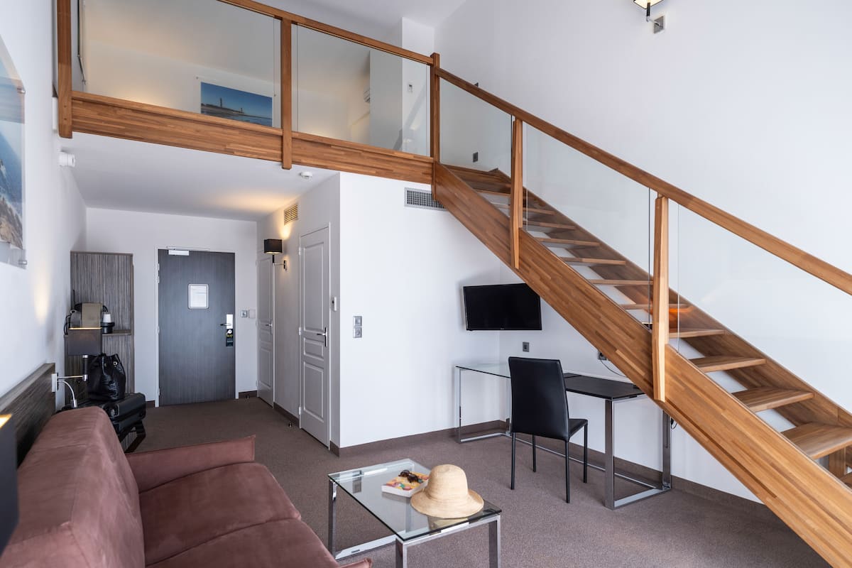 A modern living room with a wooden staircase, a glass coffee table, a leather sofa, and a flat-screen TV.