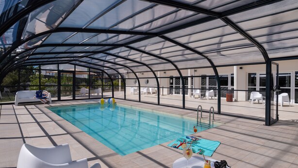 A covered swimming pool area with lounge chairs and a table with drinks.