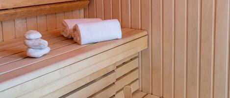 A wooden sauna with benches, a towel, and a wooden bucket with a scoop.