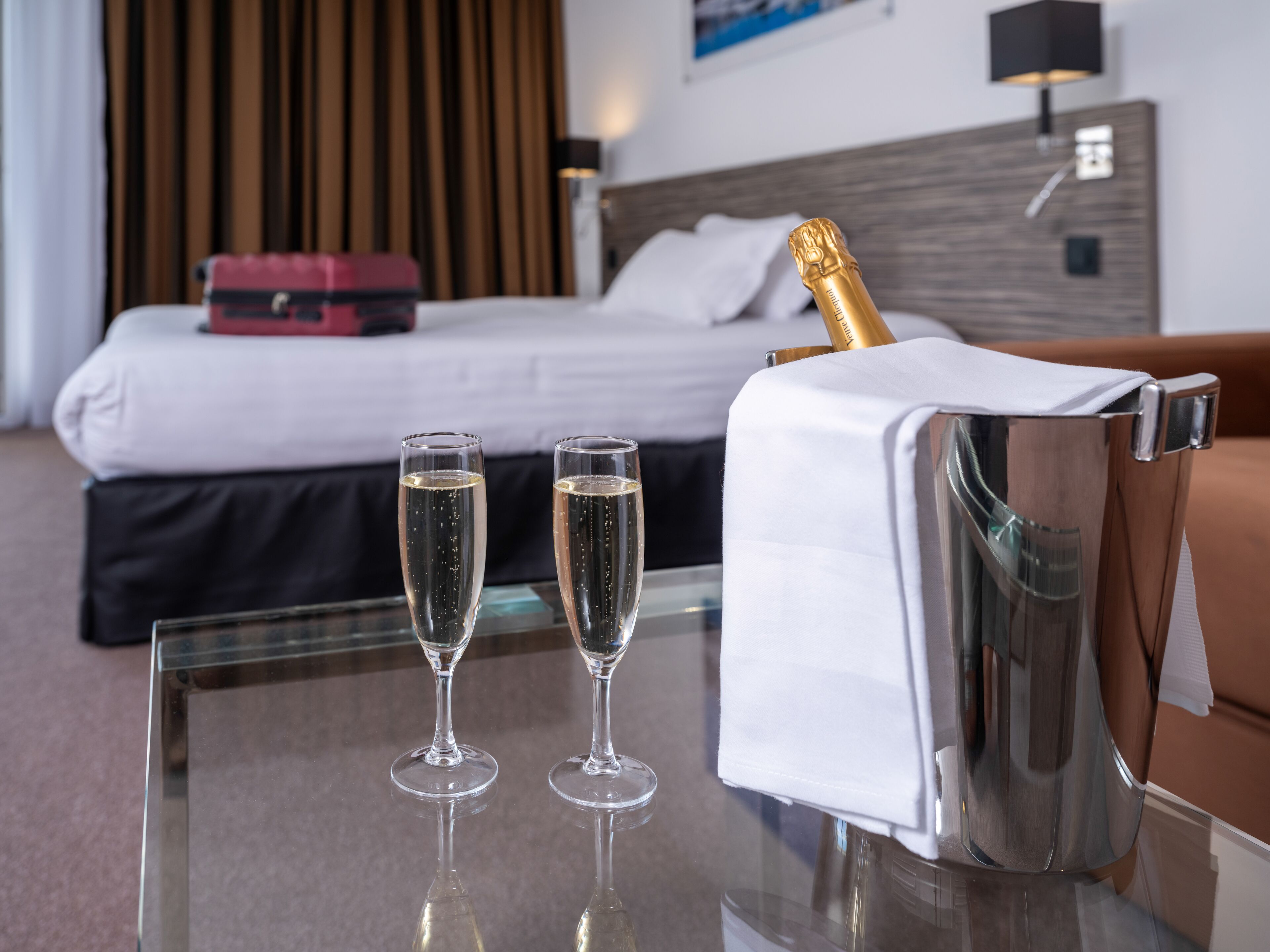 A hotel room with a bed, two champagne glasses, and a champagne bottle in a silver bucket.