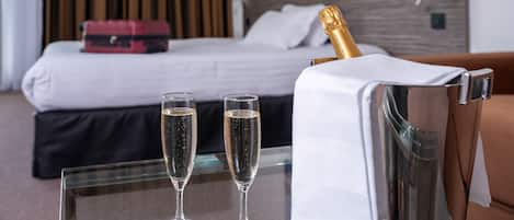 A hotel room with a bed, two champagne glasses, and a champagne bottle in a silver bucket.