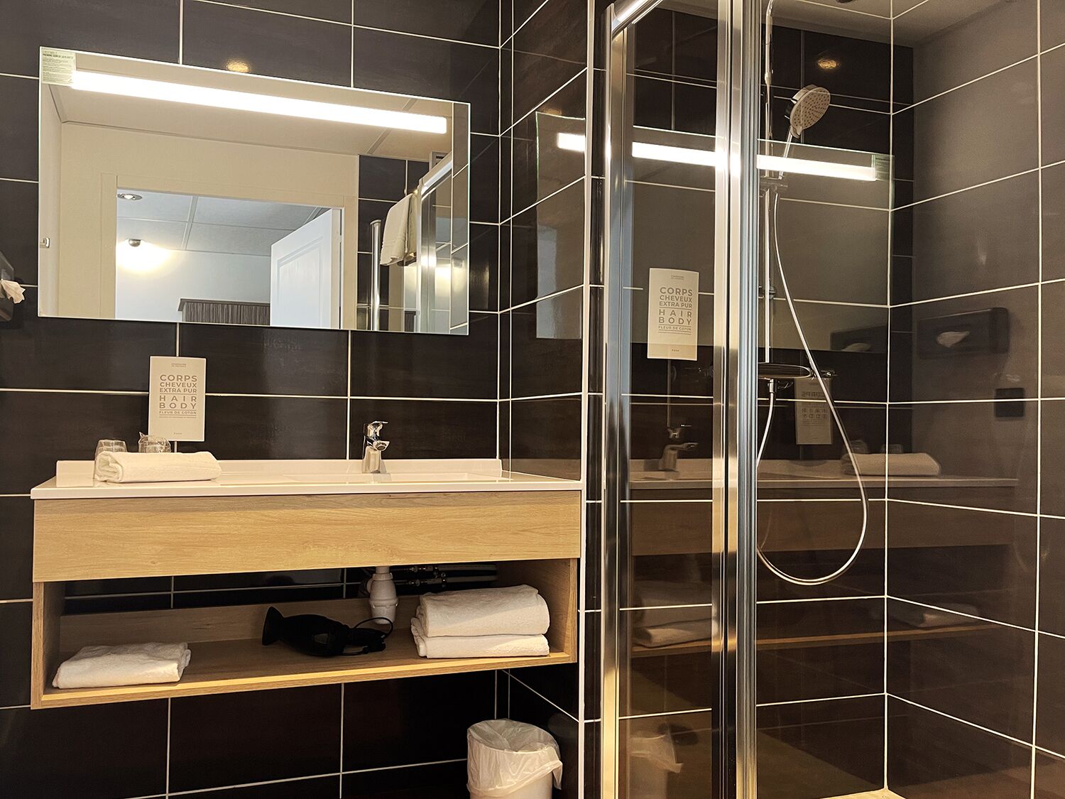 Un bagno moderno con cabina doccia in vetro, mobile bagno in legno e uno specchio grande.