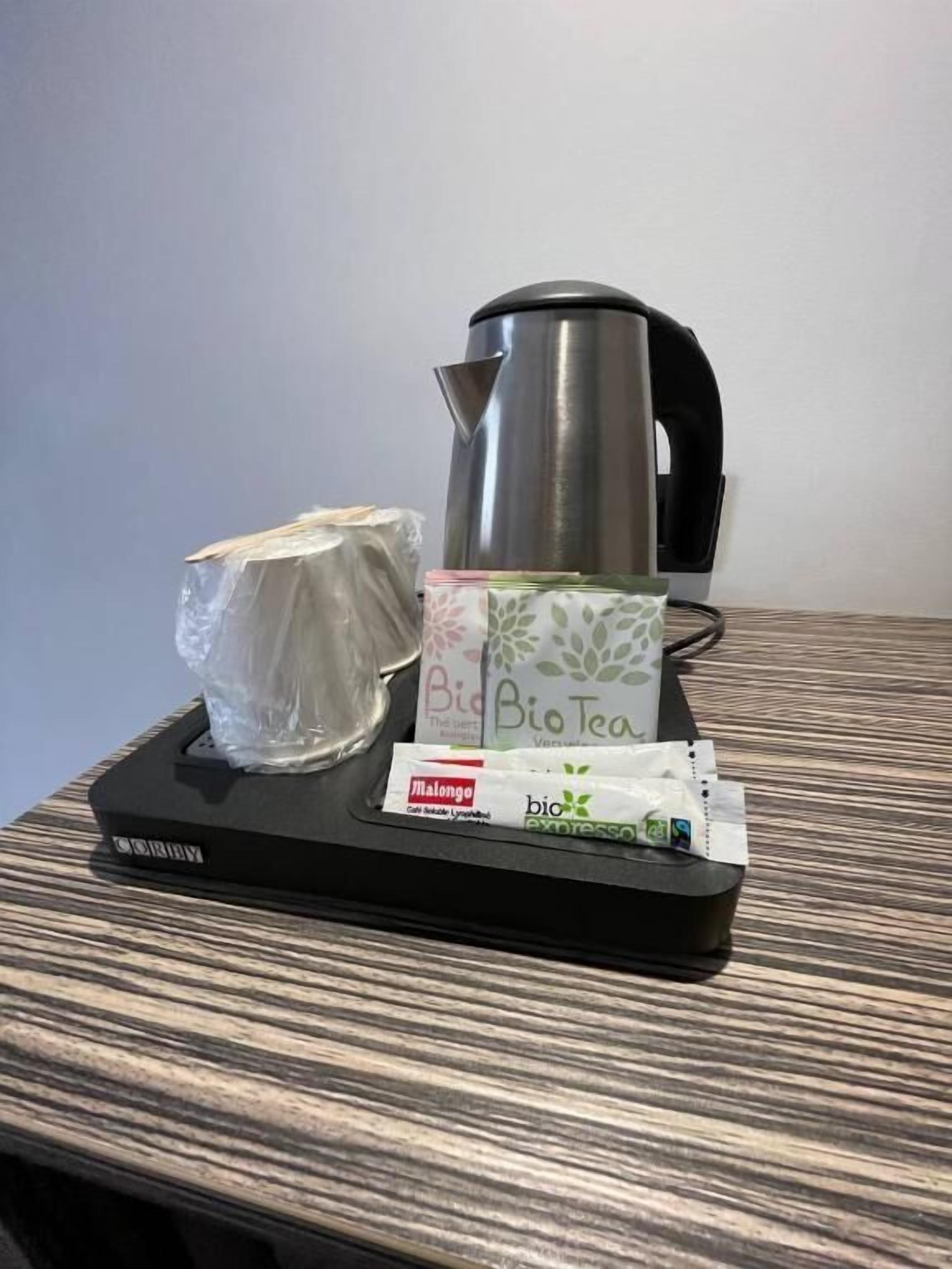 Un plateau sur lequel se trouvent une bouilloire, un objet emballé et quelques sachets de thé, le tout posé sur une surface en bois.