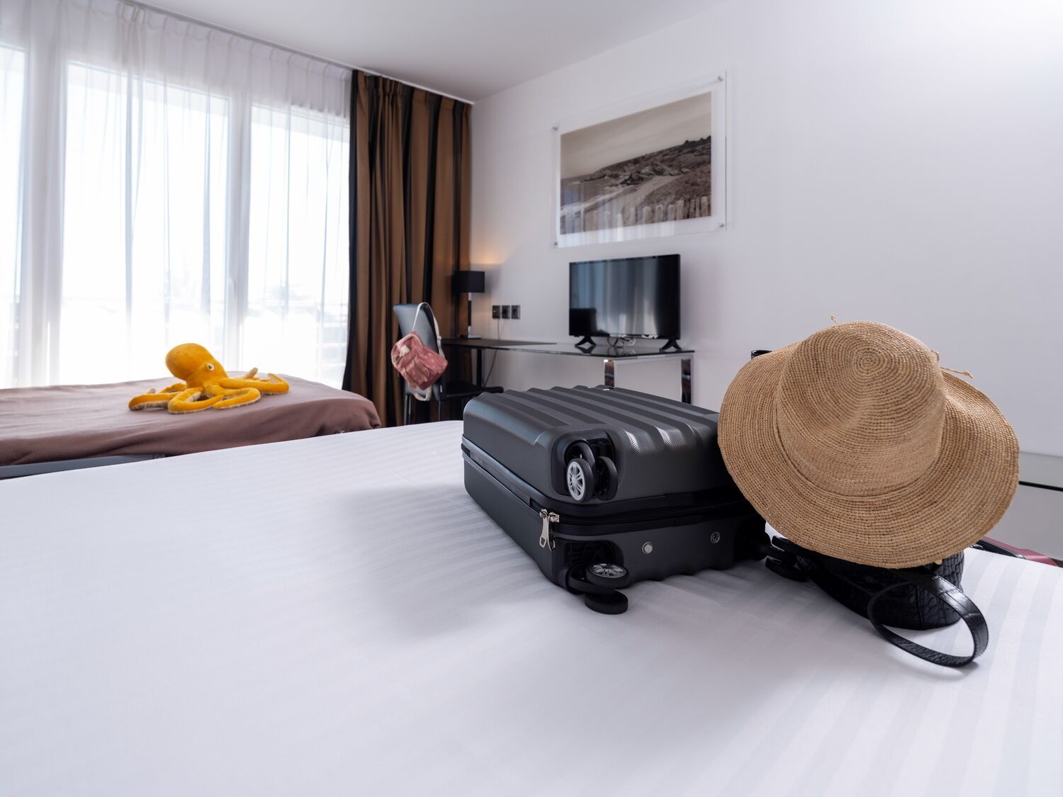 A hotel room with a bed, a suitcase, a hat, and a television.