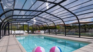 A covered swimming pool with a glass ceiling, lounge chairs, and a table with umbrellas. - Golden Tulip La Baule Hôtel & Résidence (La Baule-Escoublac)