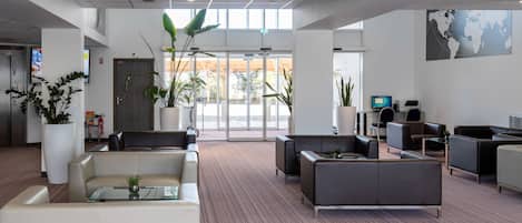 A spacious lobby with modern furniture, large potted plants, and a world map on the wall.