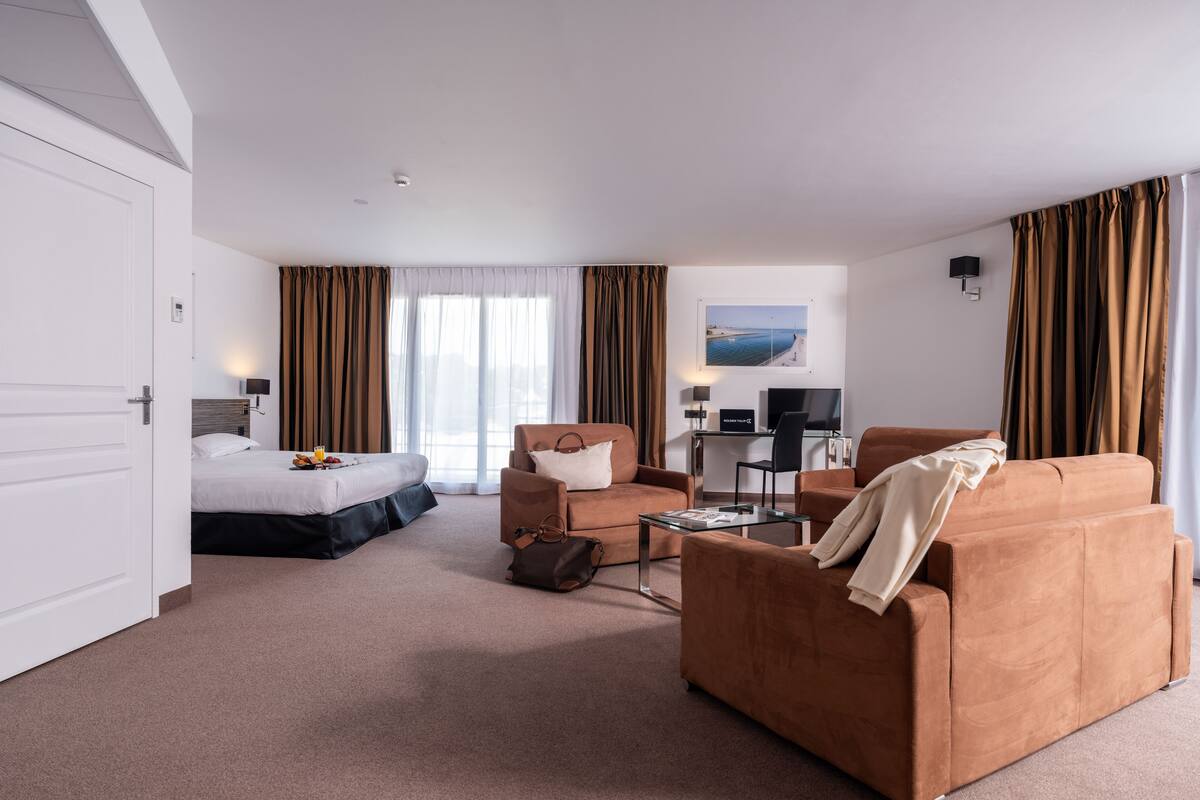 A hotel room with a bed, two sofas, a desk with a computer, and a TV.