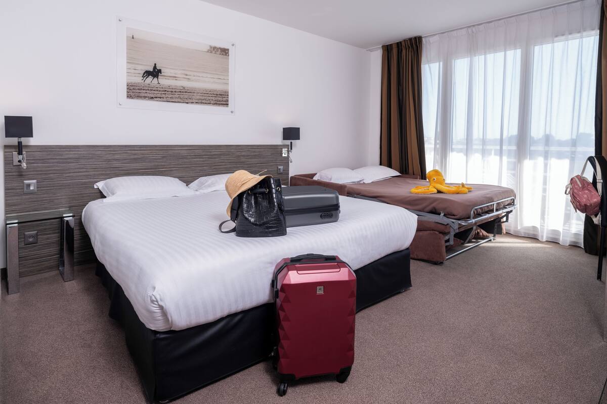 A hotel room with two beds, a red suitcase, a black handbag, and a yellow stuffed toy on one bed.