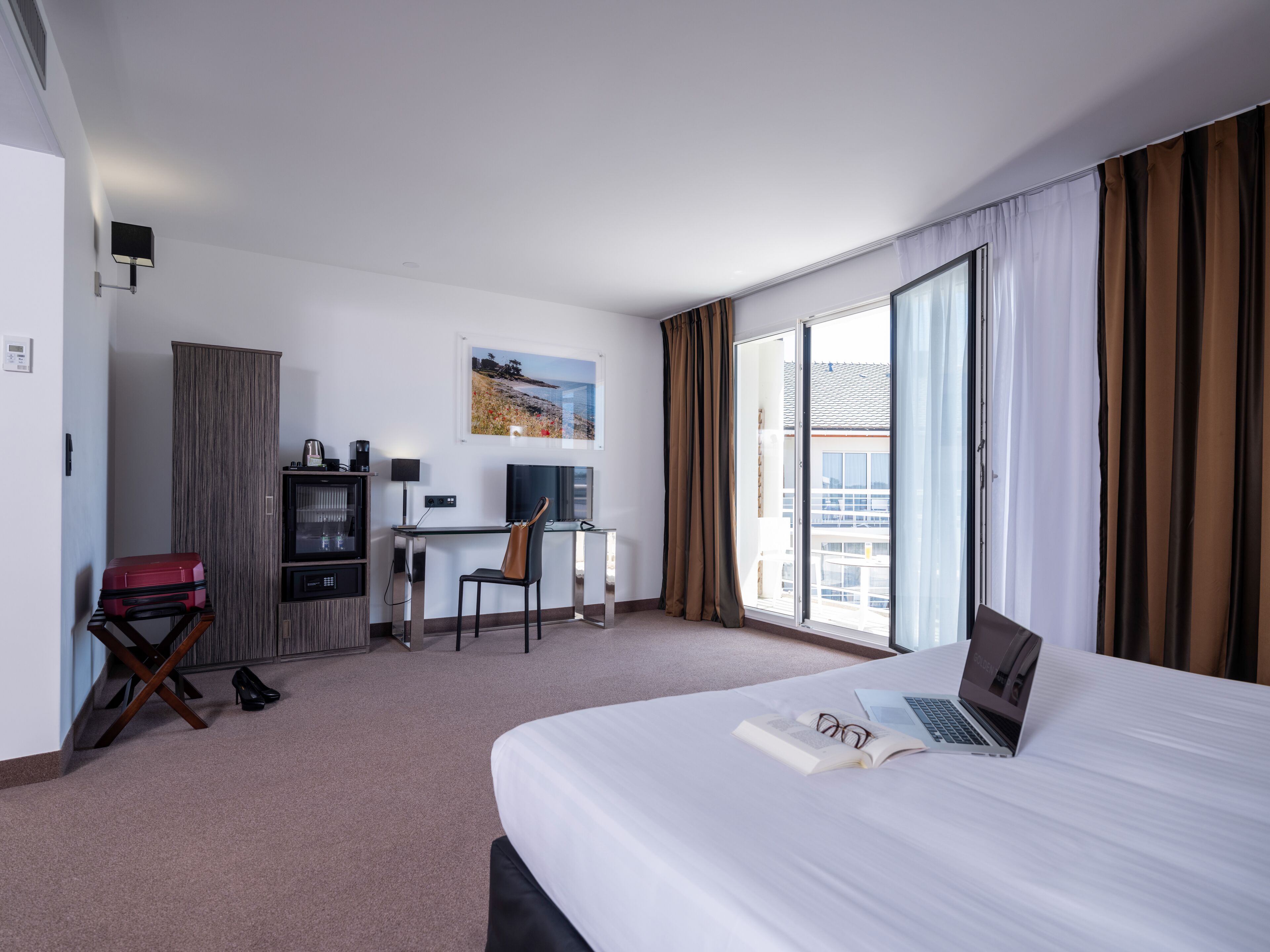 Une chambre d’hôtel équipée d’un lit, d’un bureau avec un ordinateur portable, d’une télévision et d’un mini-bar.