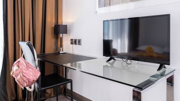 Une chambre d’hôtel moderne avec un bureau en verre, une chaise noire, un téléviseur et un tableau au mur.