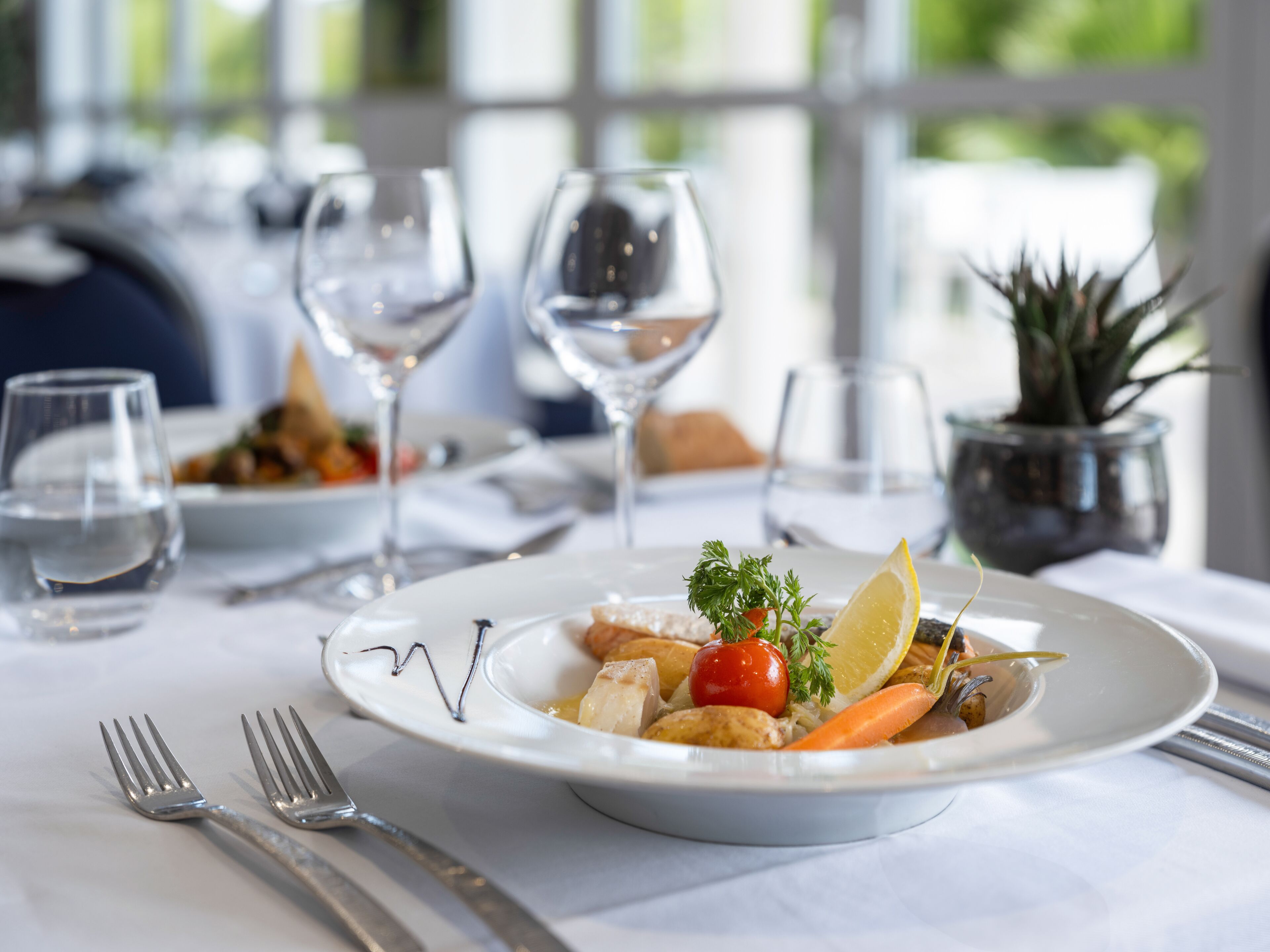 A dining table with a plate of food, wine glasses, and cutlery.