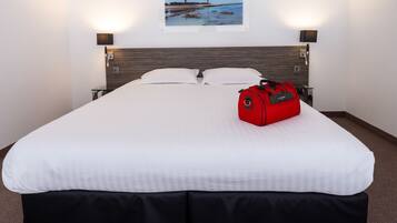 A hotel room with a large bed, a red suitcase, and a framed picture of a lighthouse on the wall.