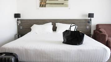 A hotel room with a bed, a black handbag on the bed, a brown chair, and a picture on the wall.