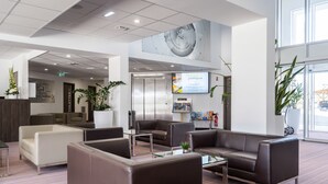 A modern lobby with leather sofas, a glass coffee table, and potted plants.
