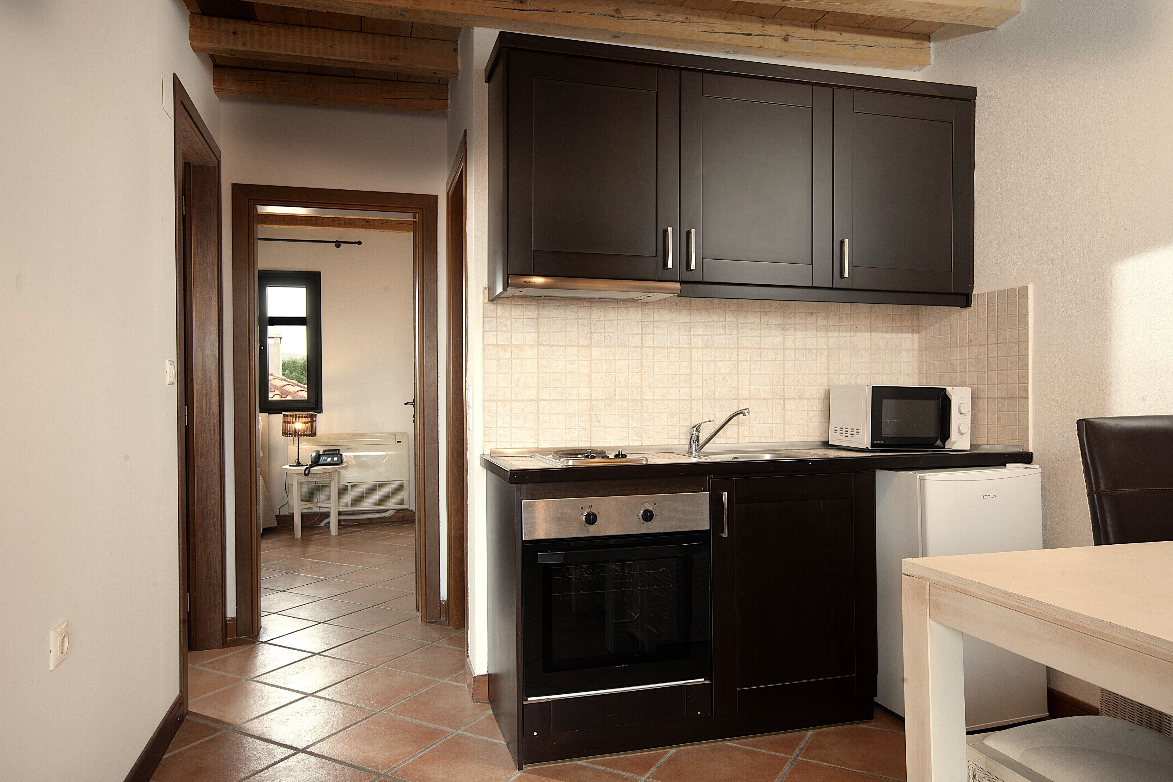 A compact kitchen with dark cabinets, a microwave, a small refrigerator, and an oven.