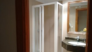 Un baño con ducha, lavamanos y espejo.
