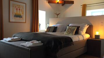 A modern bedroom with a large bed, a bedside table with a lamp, and a framed artwork on the wall.
