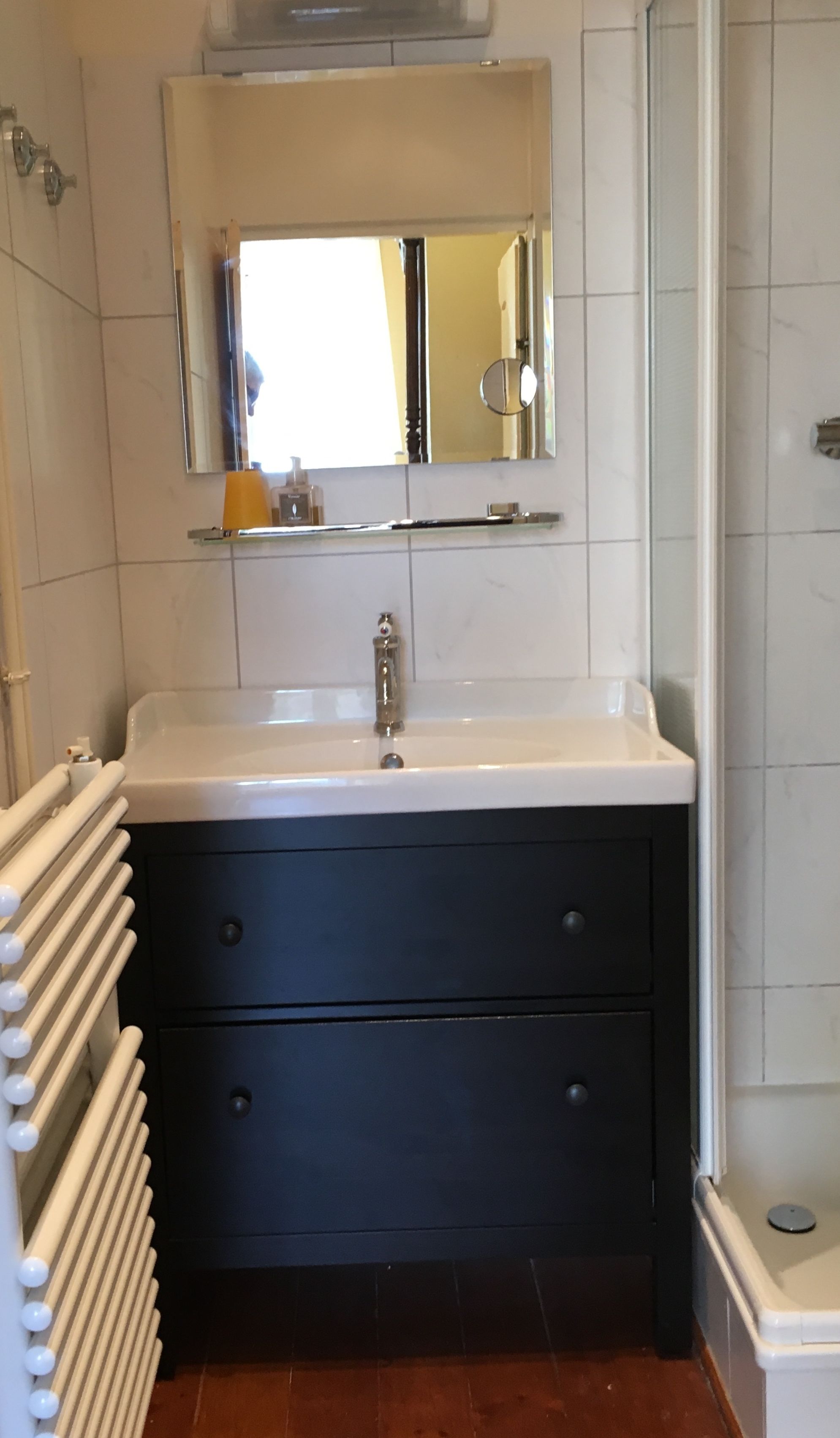 Un baño con un lavamanos blanco, un espejo encima y una zona de ducha a la derecha.