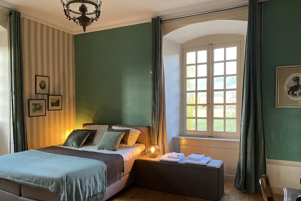 Une chambre à coucher avec un lit, une table de chevet et une fenêtre avec des rideaux.