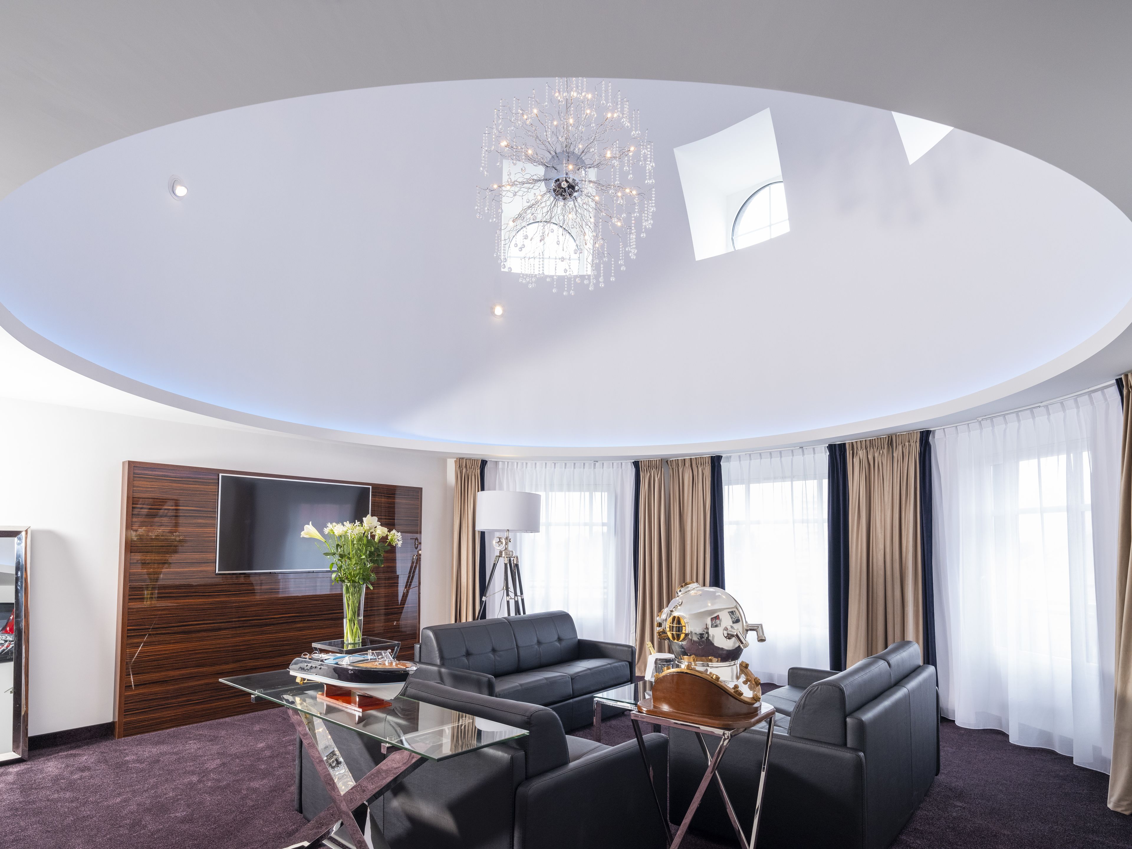 A modern living room with a curved ceiling, a chandelier, a flat-screen TV, a coffee table, and a sofa.