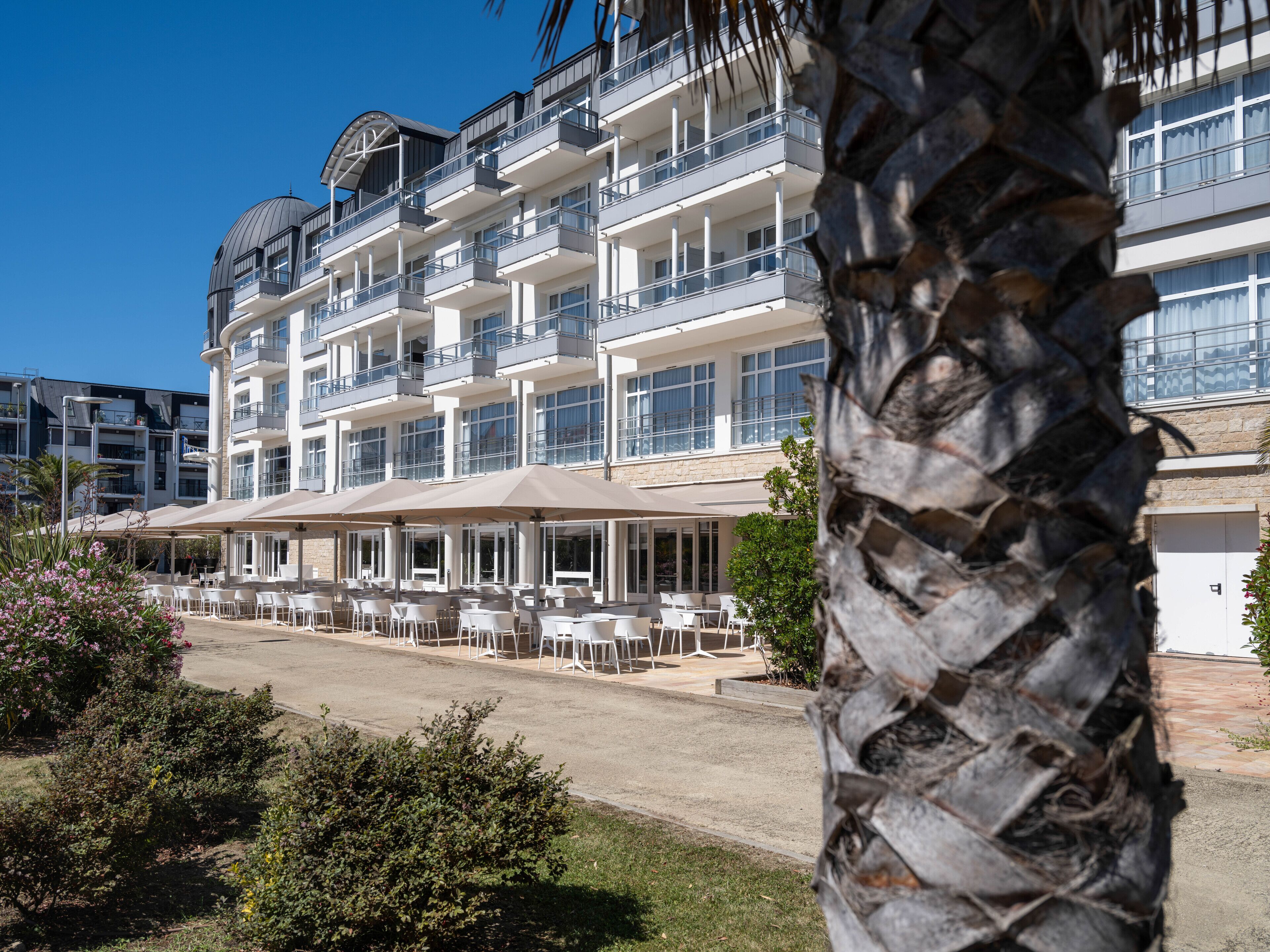 A multi-story hotel with outdoor seating and a palm tree in the foreground.