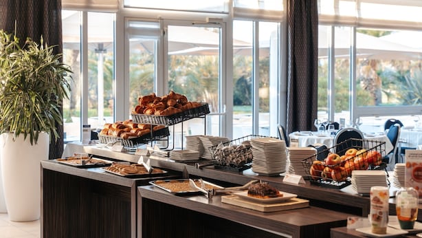 A buffet setup with various food items and a large window with a view of trees. - Westotel Le Pouliguen (Le Pouliguen)