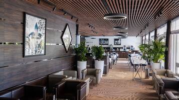 Un moderno vestíbulo de hotel con techo de madera, plantas en macetas grandes y una alfombra estampada.