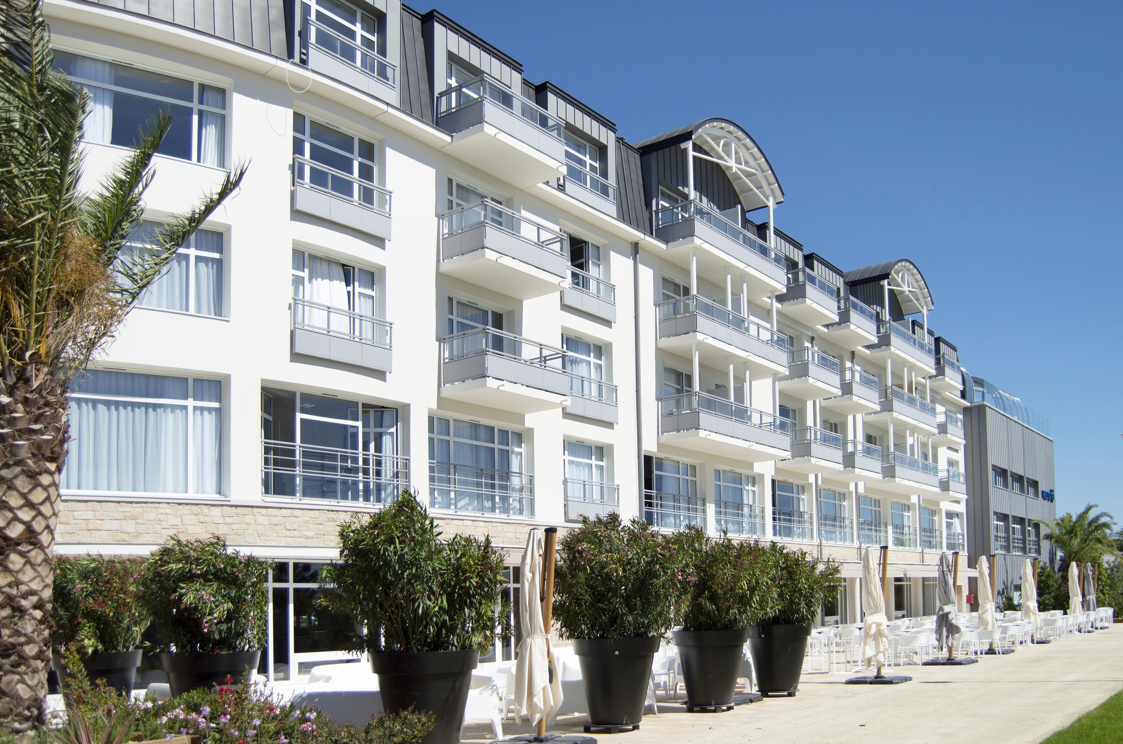 A multi-story hotel with balconies, large windows, and potted plants.