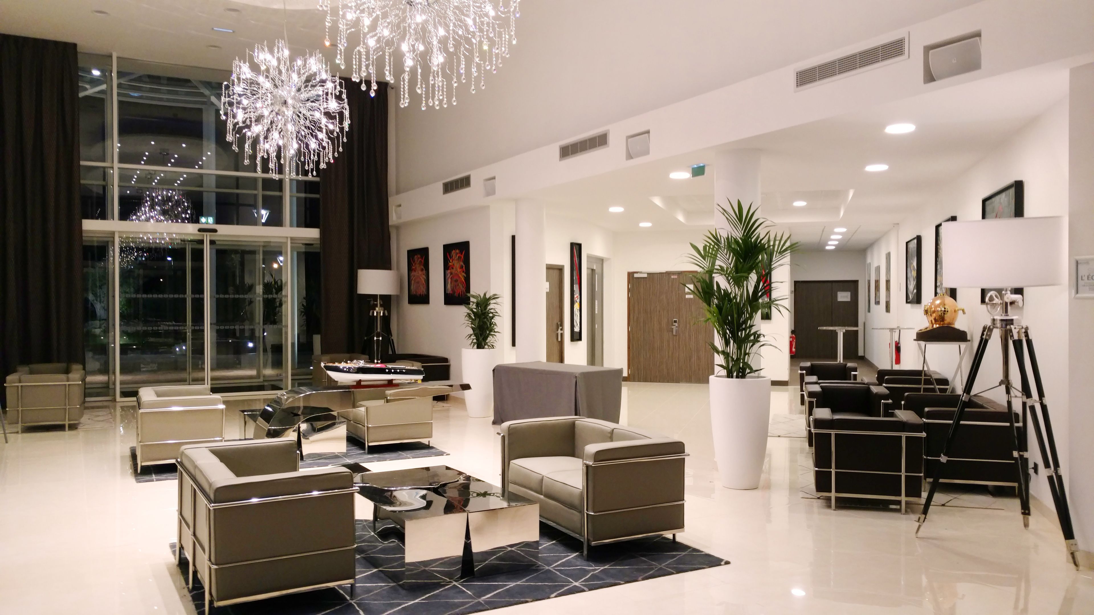 A modern lobby with a glass partition, seating area, and a large chandelier.