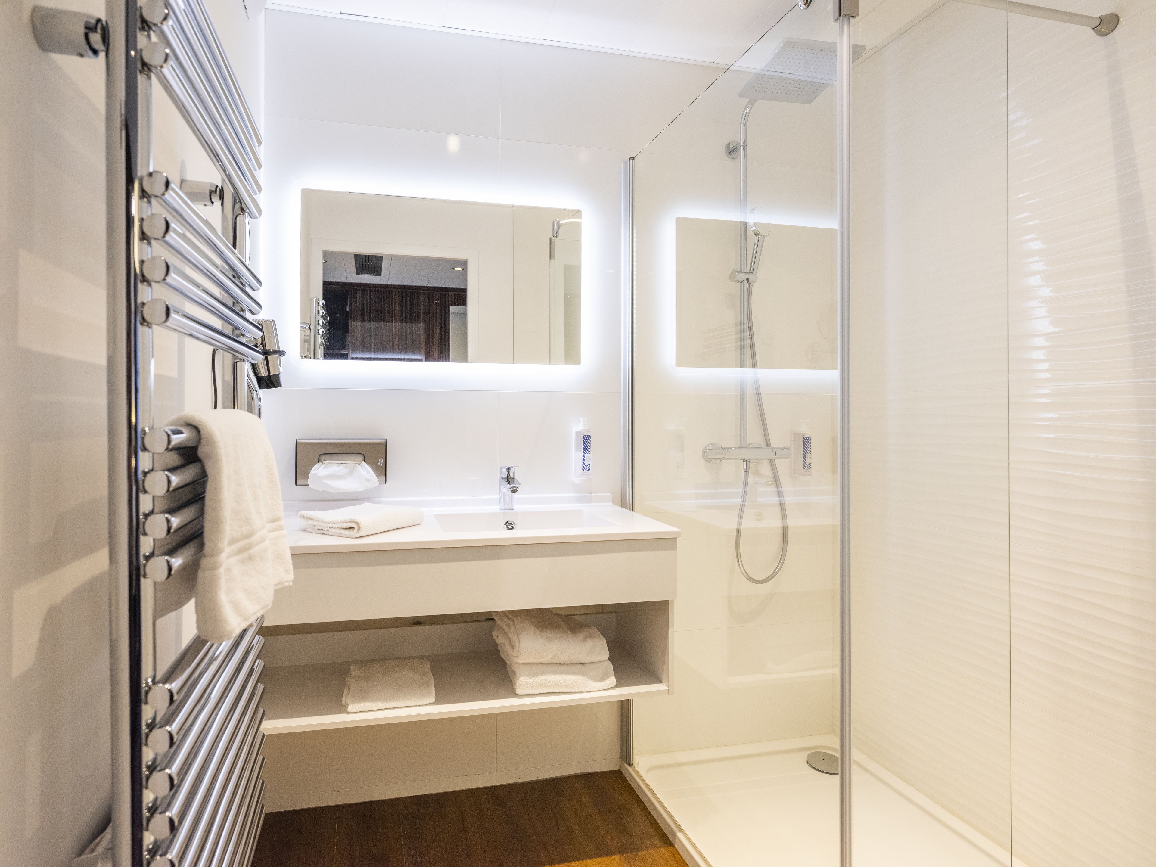 A modern bathroom with a glass-enclosed shower, a white vanity with a mirror, and a towel rack.
