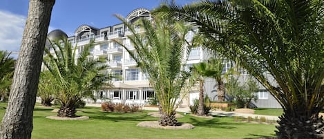 A hotel with multiple floors, large windows, and a well-maintained garden with palm trees.