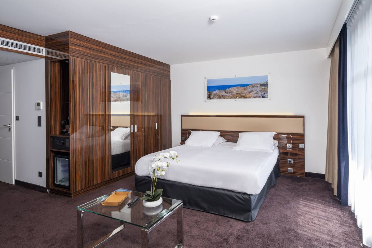 Quarto de hotel com uma cama grande, mesa de centro de vidro, guarda-roupa e um quadro na parede.